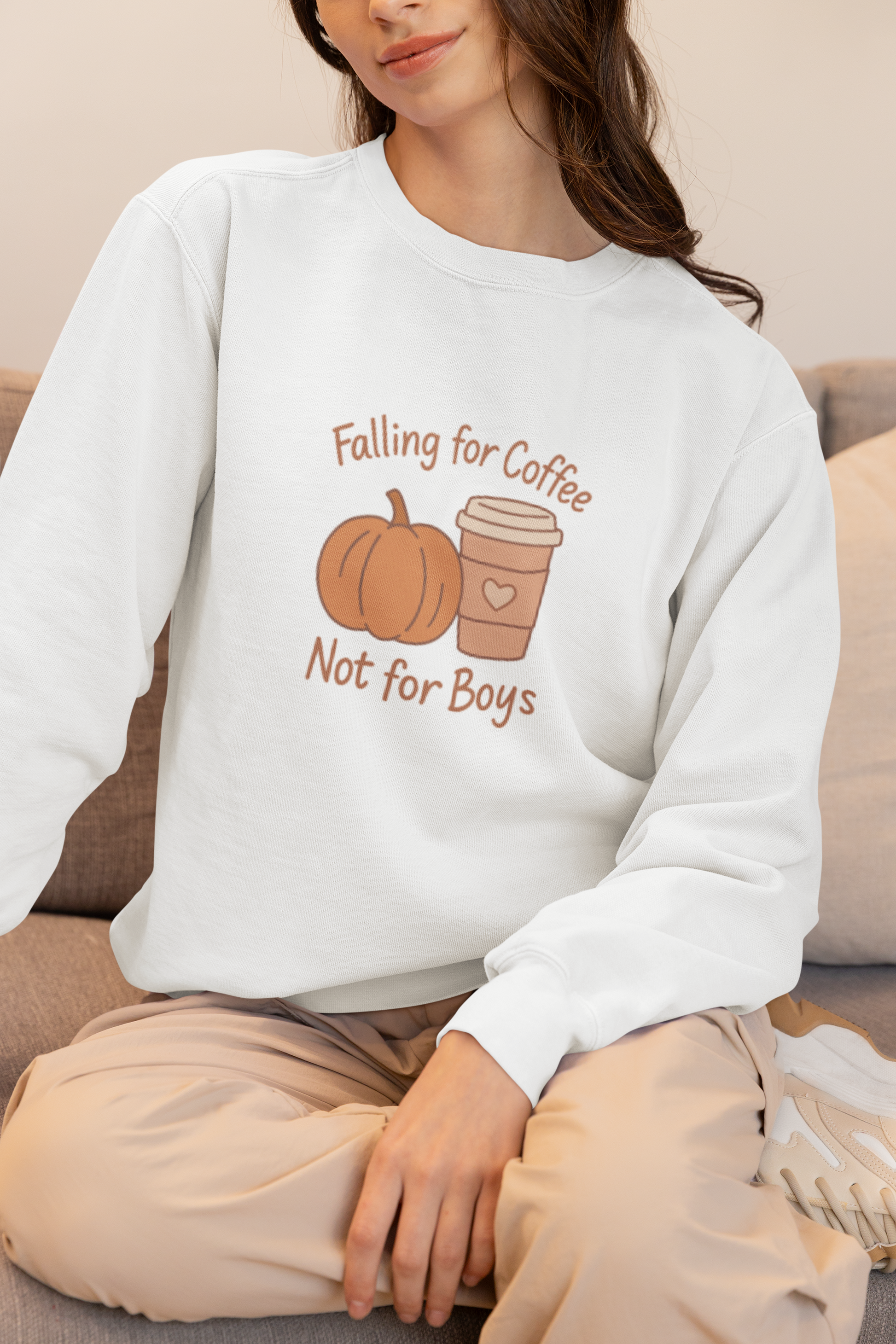 Person wearing a white sweatshirt with a pumpkin and coffee cup design, sitting on a couch.