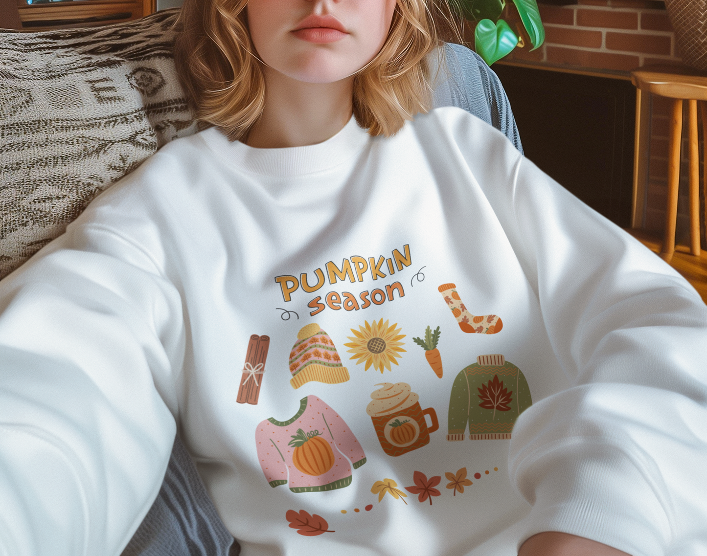 Person wearing a white sweatshirt with 'Pumpkin Season' graphics in a cozy indoor setting.